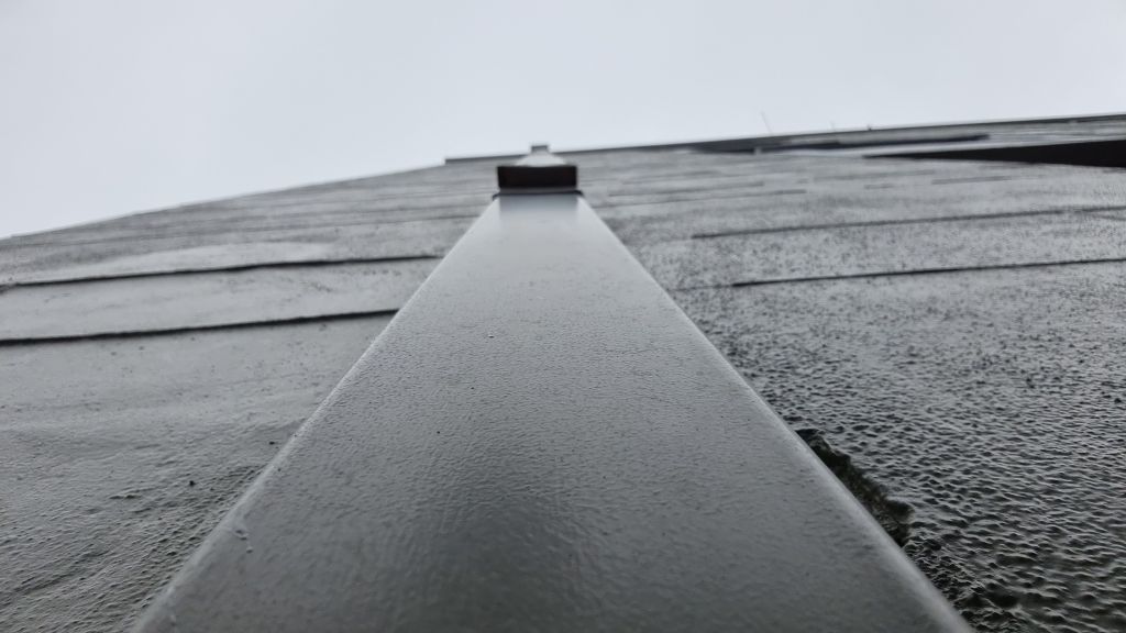 The phone is resting on the pipe of the guttering that goes to the drain. The view is looking up towards the roof, the sky is grey and the rain has just stopped.
